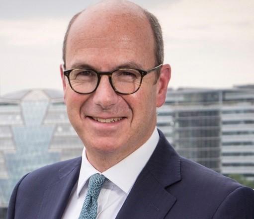 A man with a mostly bald head, glasses and a navy suit and blue tie