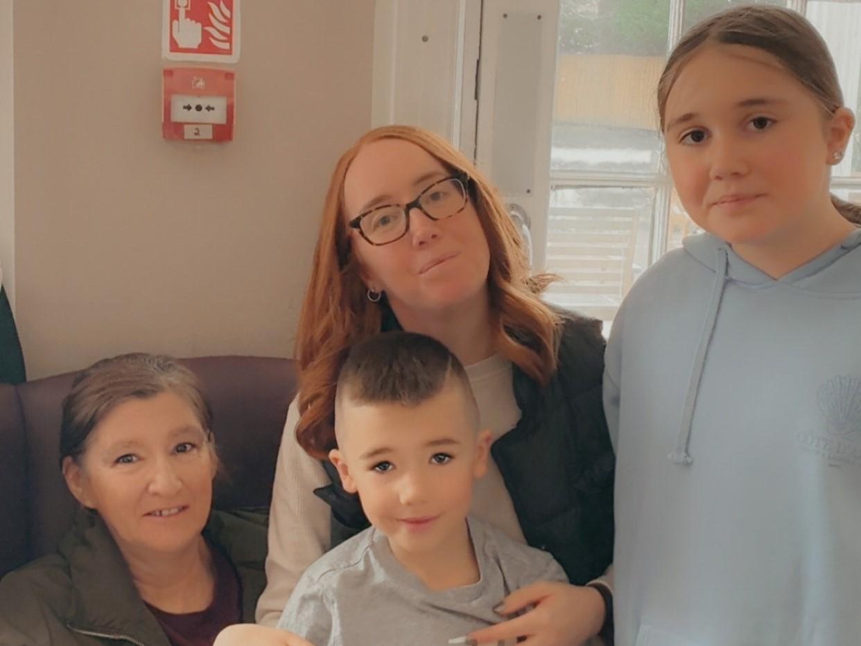 An older woman in a chair, next to her is her adult daughter, grandson and granddaughter