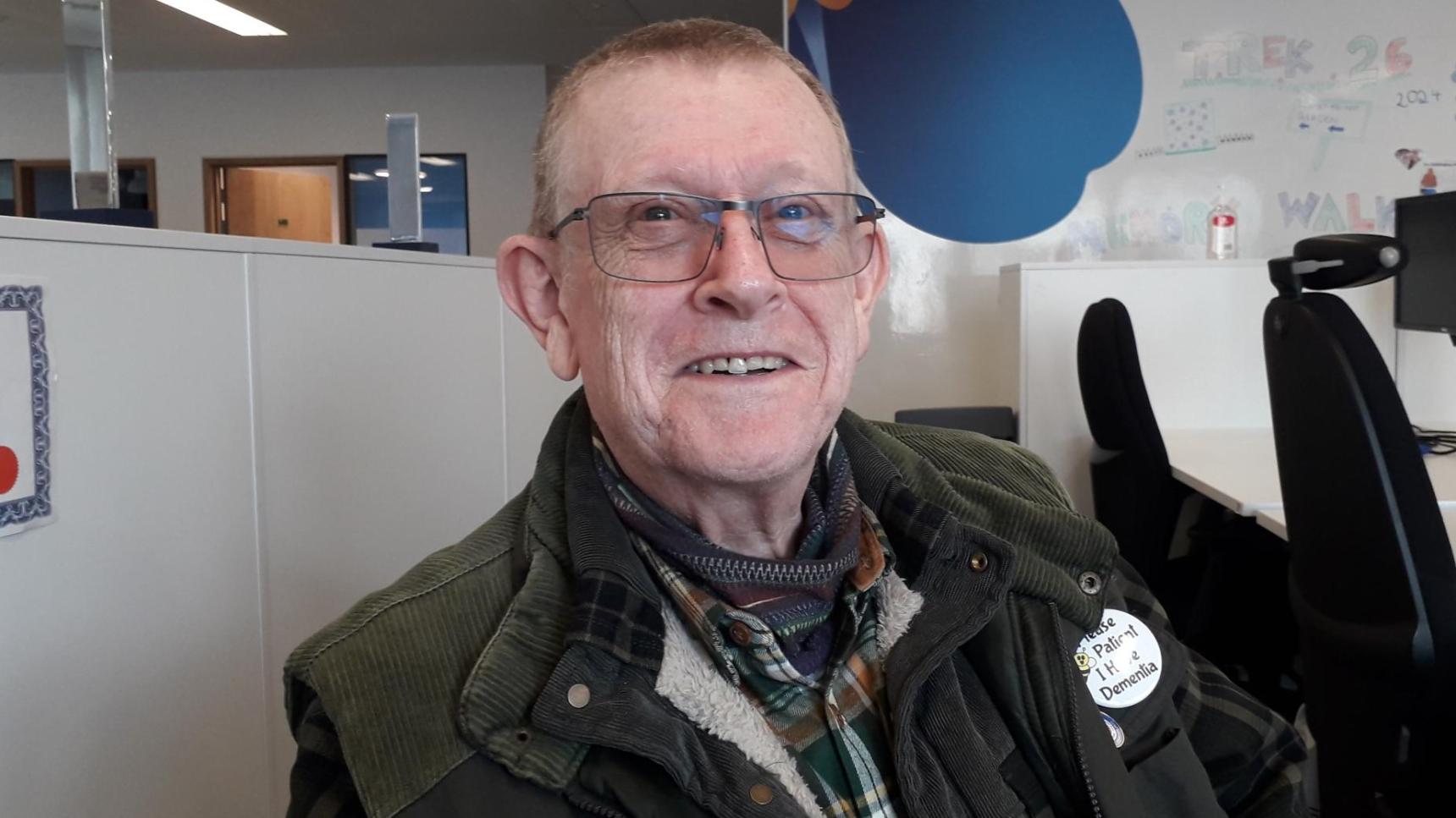 An almost bald man with glasses sat in an office, smiling
