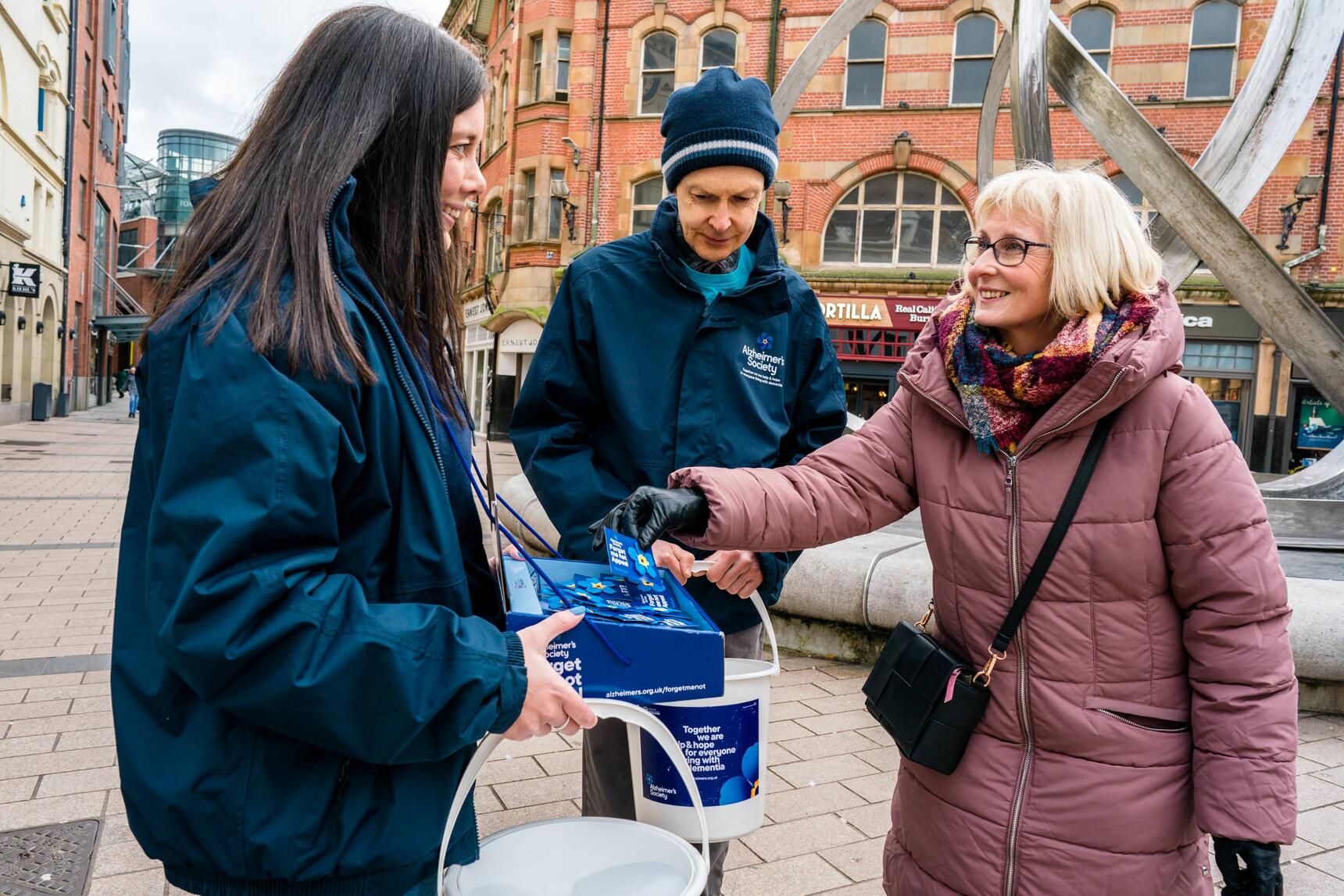 Two Alzheimer's Society with buckets and a woman donating 
