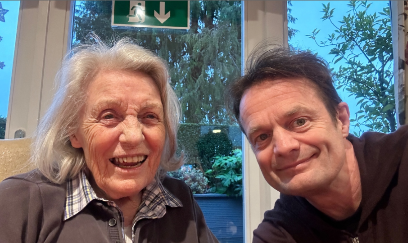 An older woman with a grey bob and a man with brown hair smiling while taking a selfie