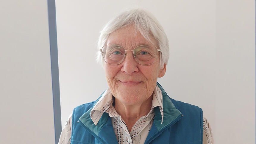 Sue has cropped grey hair, glasses and she's wearing a white shirt and turquoise gilet