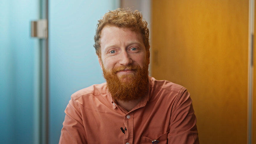 Chris has is wearing a peach-coloured shirt, he has red hair and a beard.