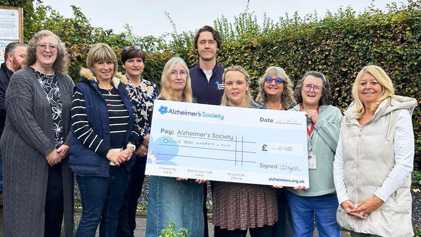 Volunteers from Olive Tree Cafe stood outside holding a big cheque.