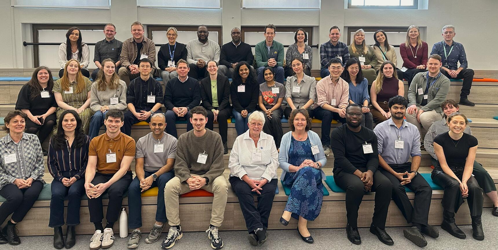 A group of people with name tags sit on benches in a hall