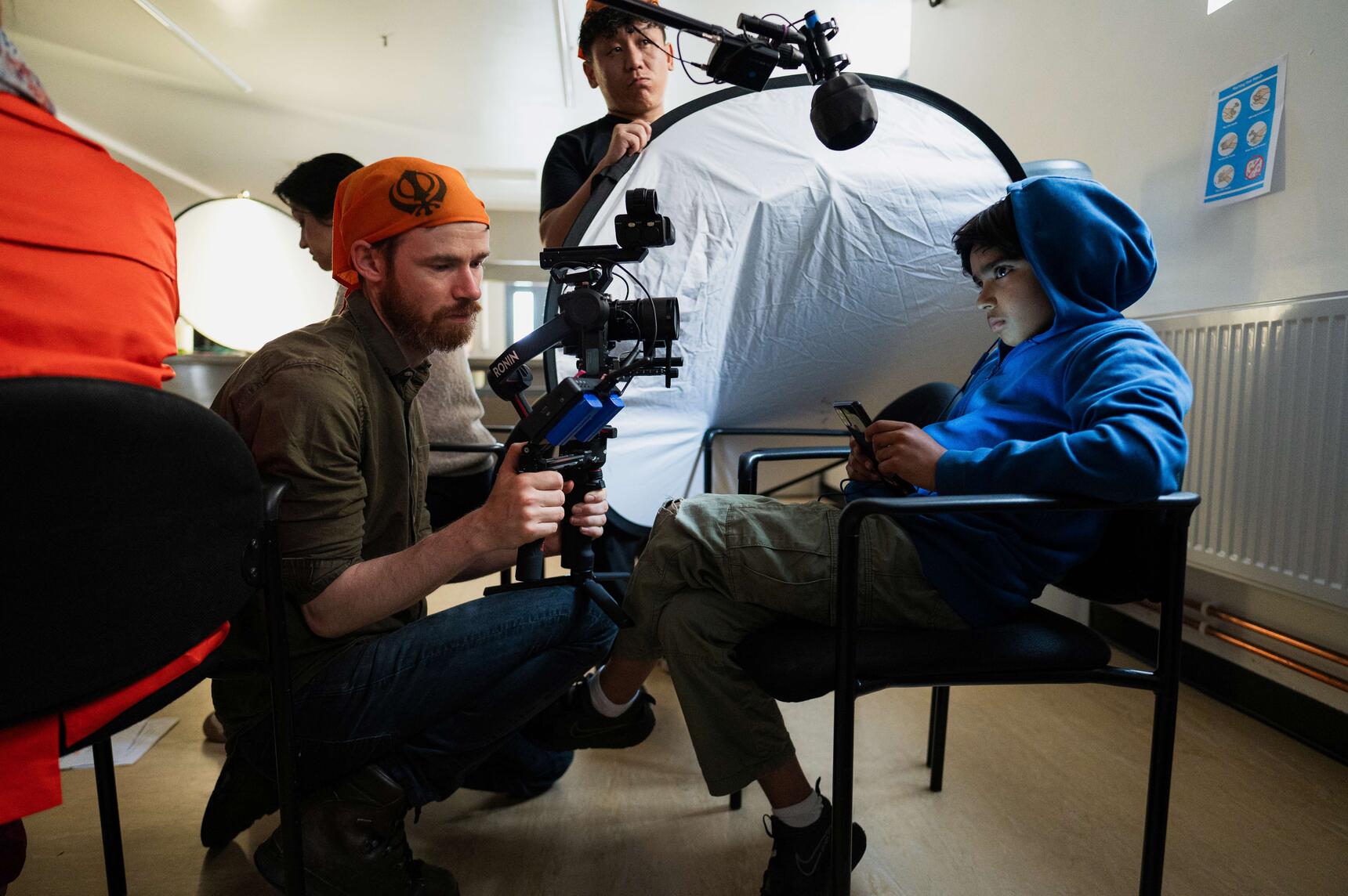A young actor sat in front of a camera and crew