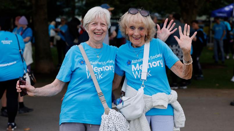Two women in blue t-shits smiling and waving 
