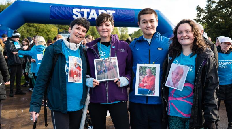 Group of 4 people in Memory Walk t-shirts, smiling and holding pictures of a loved one.
