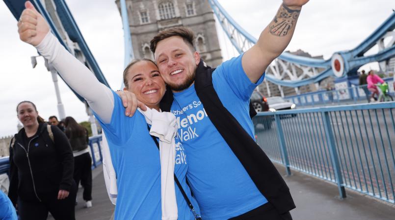 2 people wearing blue Memory Walk t-shirts, hugging and smiling with their arms in the air