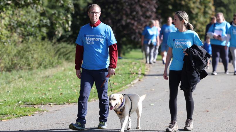 Two people in blue Memory Walk t-shirts, walking with a dog.