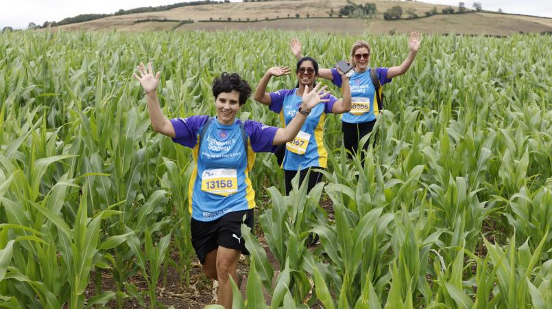 Three women waving and walking through long grass.