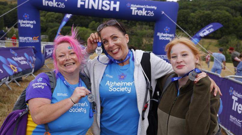 Three women with face paint smiling in front of a finish gantry.