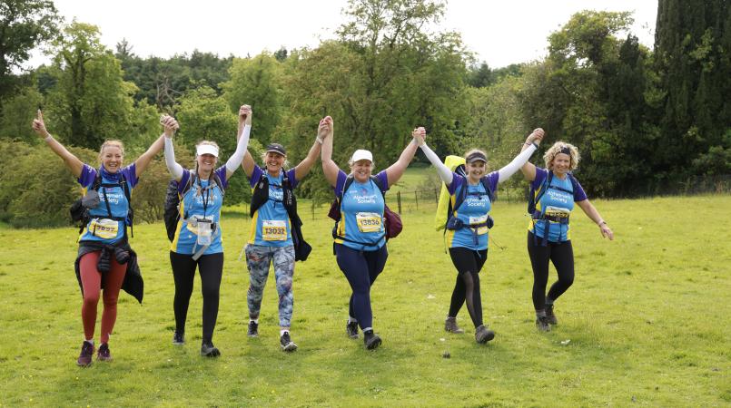 Group of women walking on a grassy field holding hands in the air.