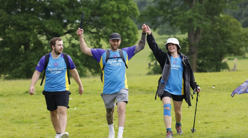 Three people walking on a green field.