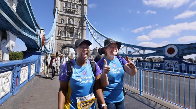 Two women walking across Tower Bridge smiling.