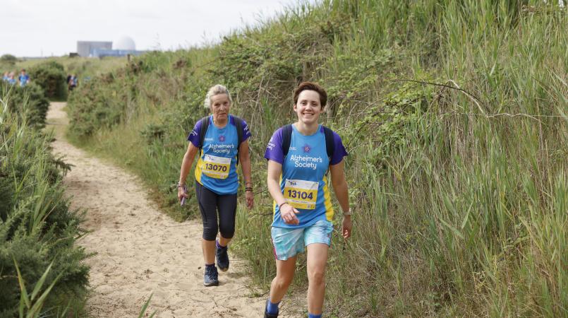 Two women walking on a sandy path.