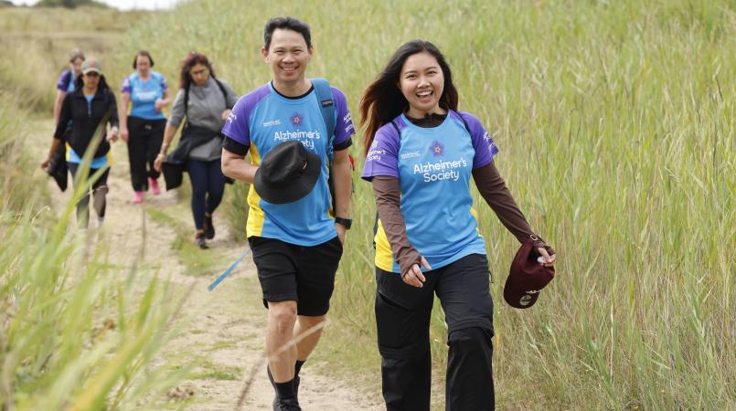 A couple walking through a field of grass smiling.