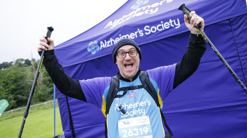 Man with a beanie hat and walking poles cheering.