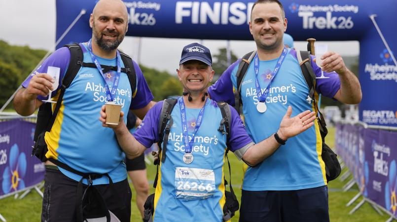 Three men smiling with medals at a finish line.