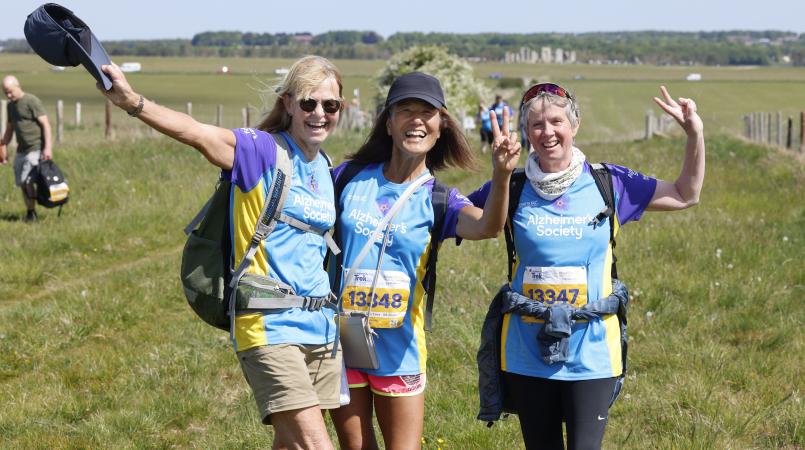 Three women smiling with Stonehenge in the background.