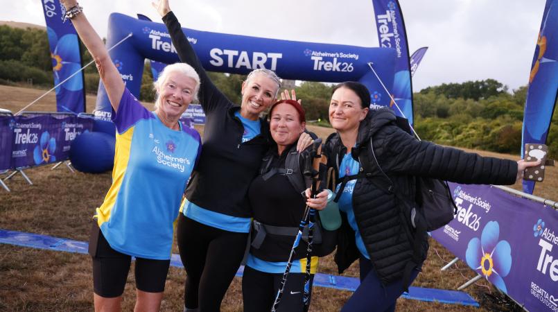 Four woman smiling with their arms raised in front of a start line.