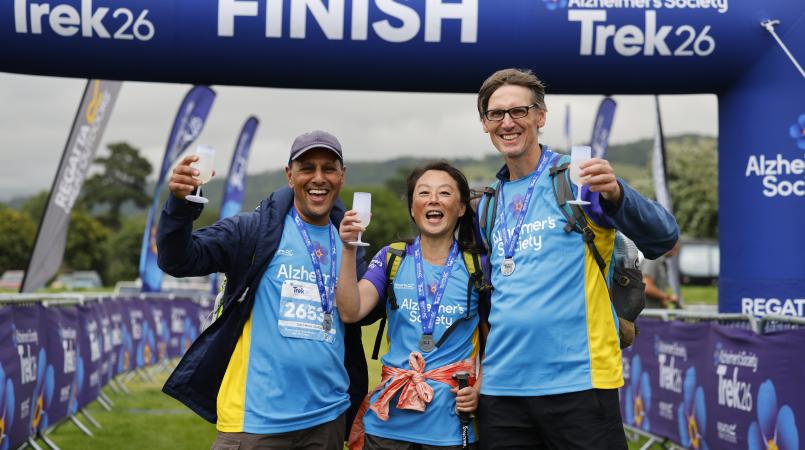 Three people smiling in front of a finish line with medals and prosecco.