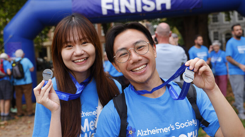 Two walkers smile and hold up their Memory Walk medals at the finish line