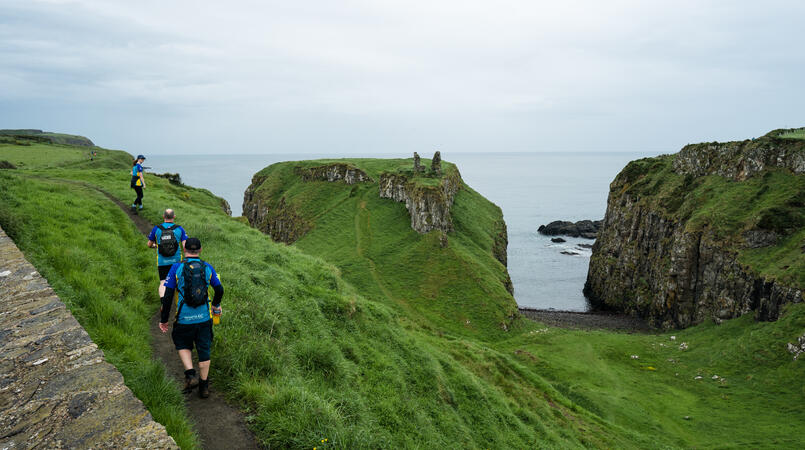 People walking away from the camera along a cliff above the water.