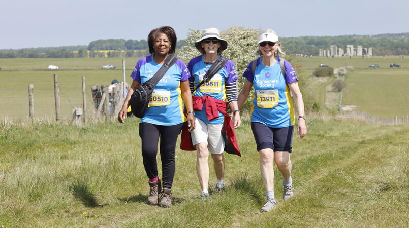 Three women smiling with Stonehenge in the background.