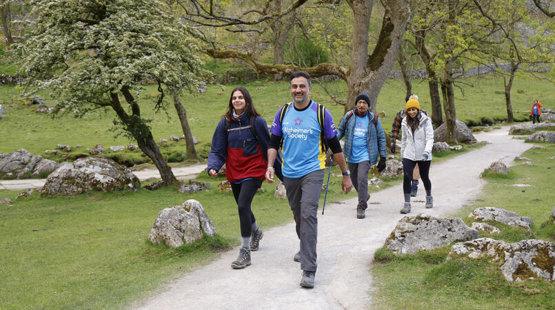 A group of people smiling while walking along a path with trees.