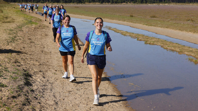 A group walking towards the camera in a line next to water.